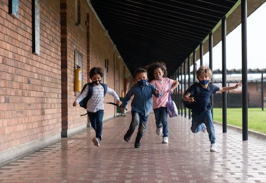 Young kids wearing masks running down a school hallway