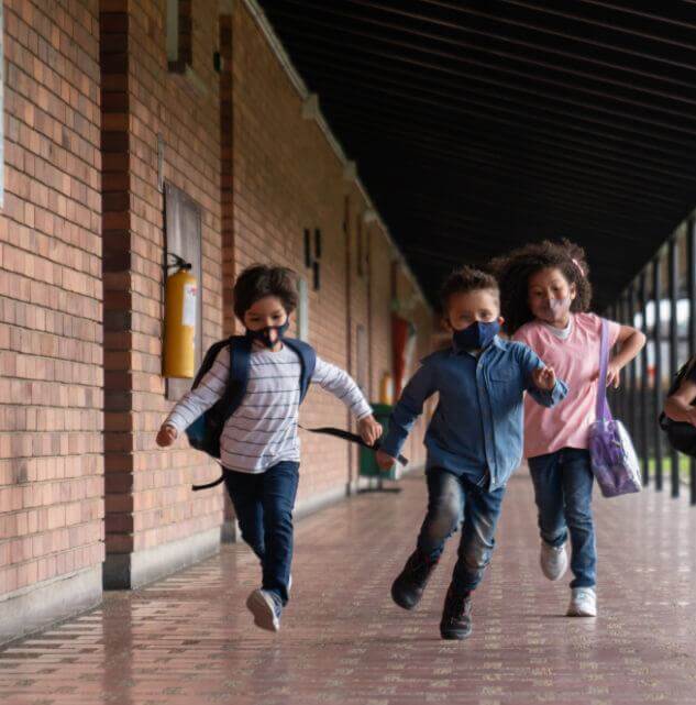 Young kids wearing masks running down a school hallway