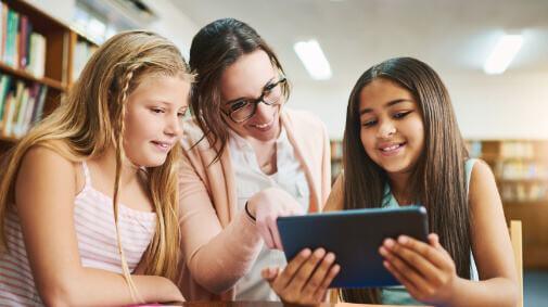 Two girls with their teacher looking at an iPad