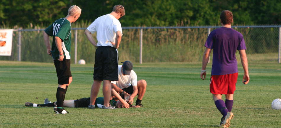 Two coaches are assessing a student athlete for a concussion on a soccer field.